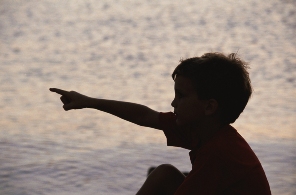 little boy sitting near the ocean and pointing